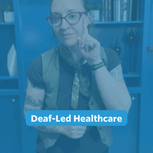 A nonbinary person with long, curly brown hair pulled back stands in front of the camera. Behind them is a blue built-in bookshelf wall. They are wearing black pants, a black shirt layered with a forest green vest, a mixed green neck bandana, and a pair of gold and green earrings. They are signing, 'deaf'.